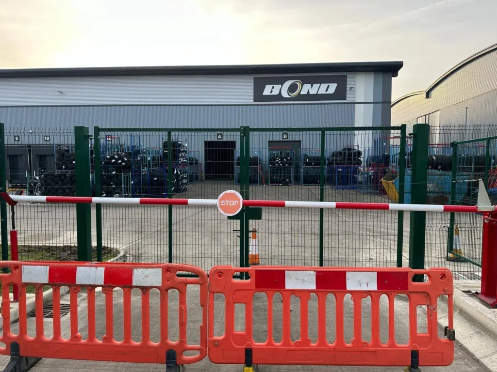 New green mesh double gates at the entrance to Bond International in Biggleswade, with the barrier arm behind
