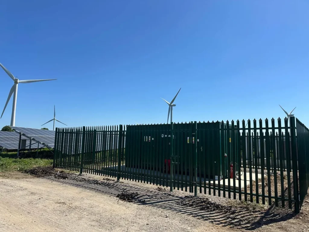 Green palisade security fencing around electrical equipment at Coldham Solar Farm