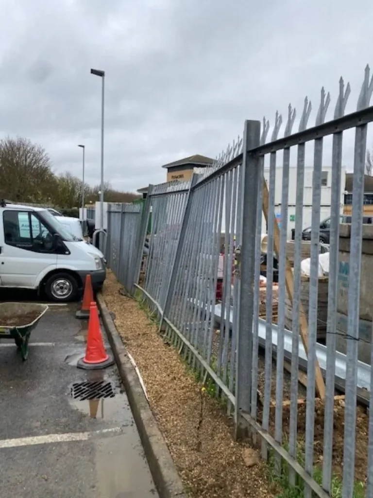 Damaged galvanised palisade on the shared boundary at the Kettering self storage site, coned off for repair